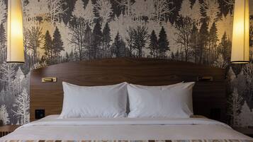 Ein Hotelzimmer mit einem Holzkopfende, zwei weißen Kissen, einer gemusterten Bettdecke und einem Wandpapier mit Waldbildern.