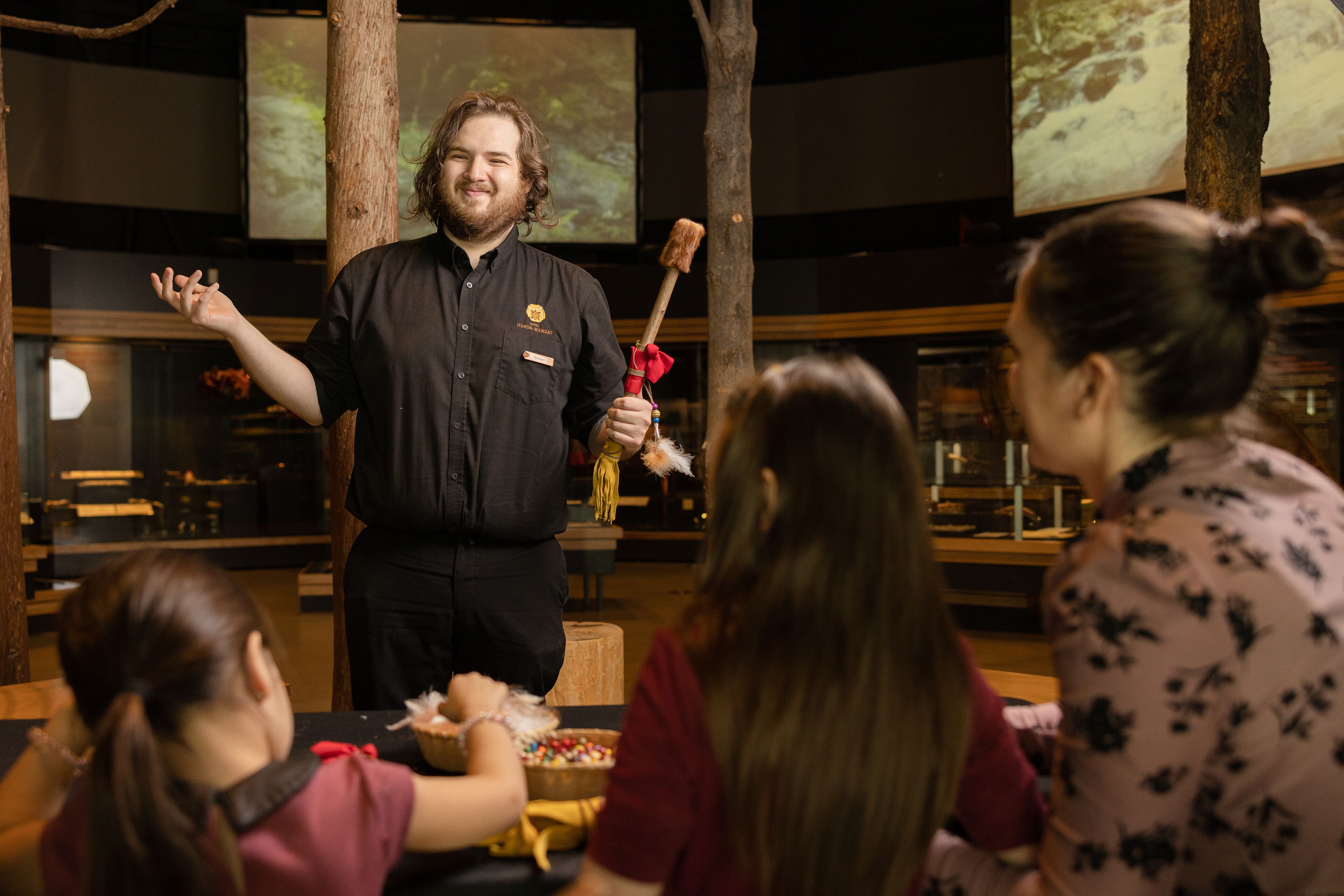 A person standing in front of an audience, holding a stick with a red feather.