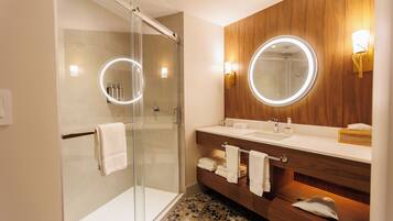 A modern bathroom with a glass-enclosed shower, wooden vanity, and two wall-mounted mirrors with illuminated frames.