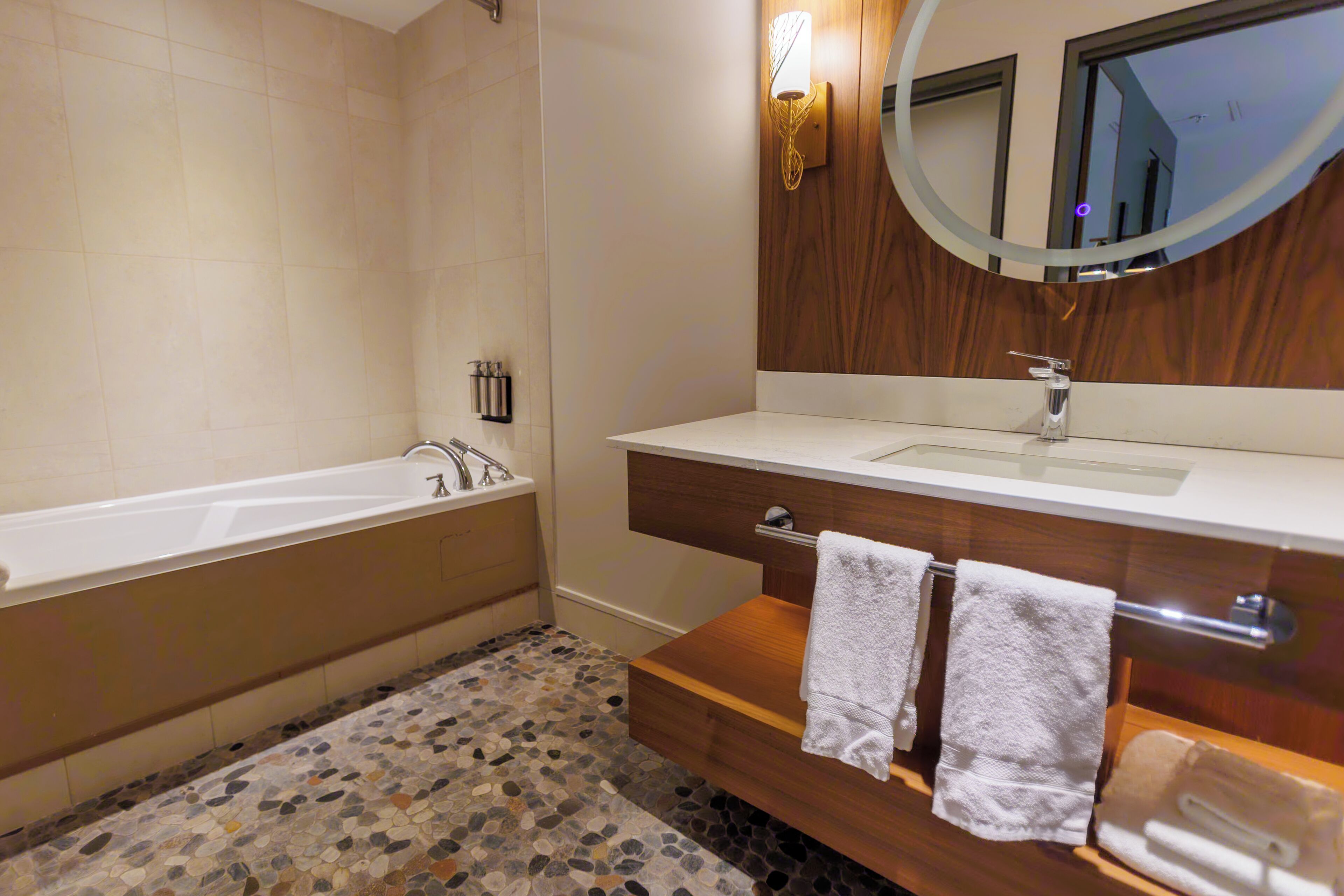 A bathroom with a bathtub, a wooden vanity with a mirror, and a mosaic floor.