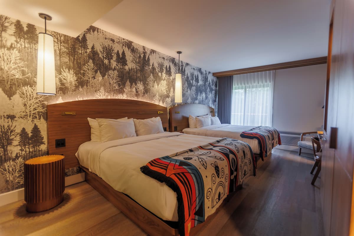 Habitación de hotel con dos camas, un mural grande en la pared y una ventana con cortinas.