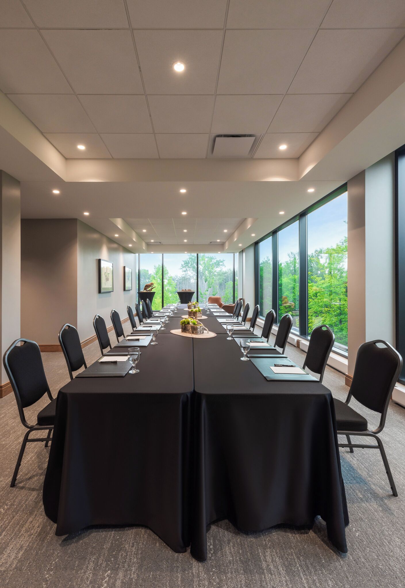 Une salle de conférence dotée d’une longue table, de chaises noires et de grandes fenêtres donnant sur un paysage verdoyant.