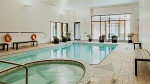 Piscina interior com água cristalina, rodeada por cadeiras de lounge pretas e plantas em vasos.