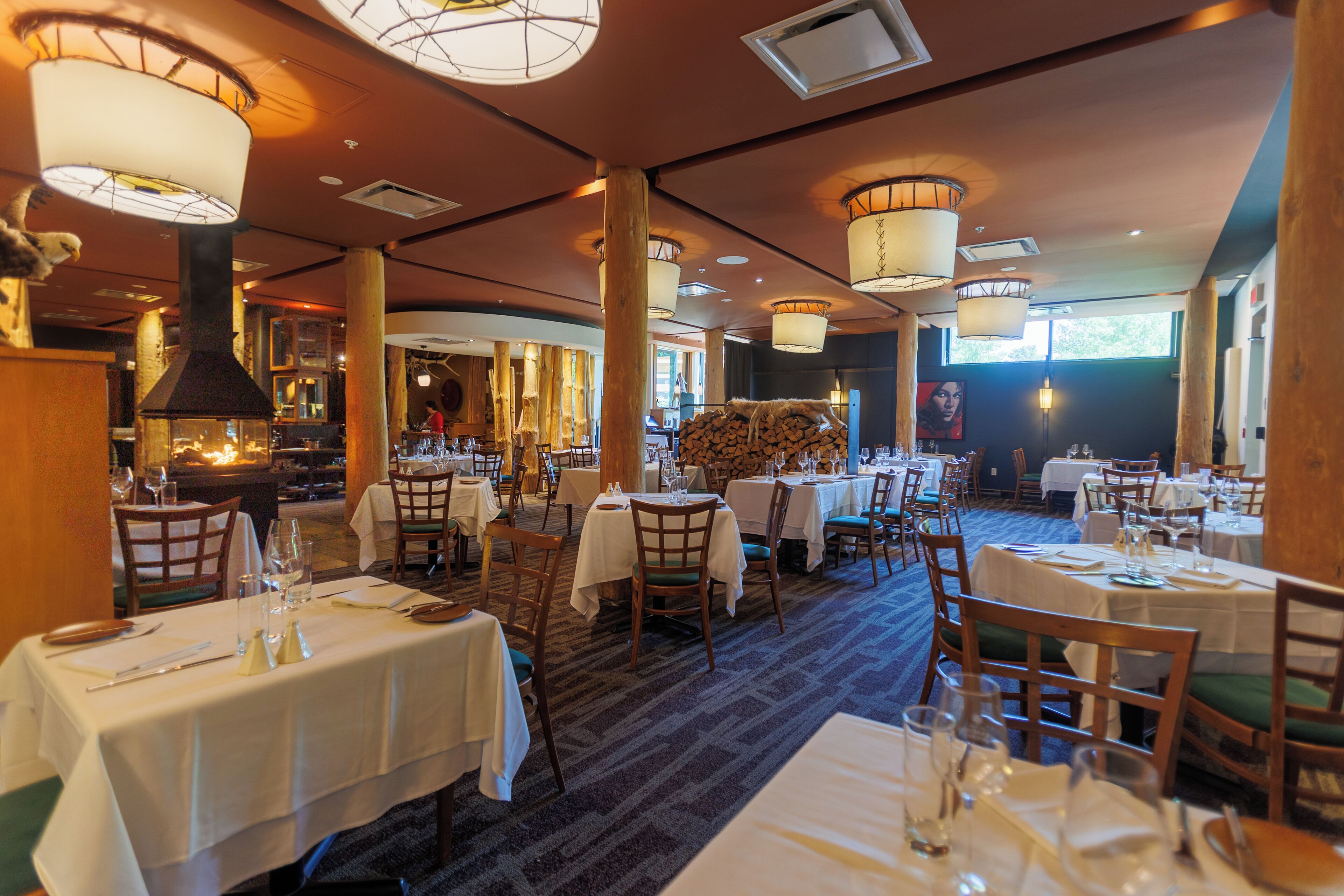 A restaurant with round tables, chairs, and hanging lamps.