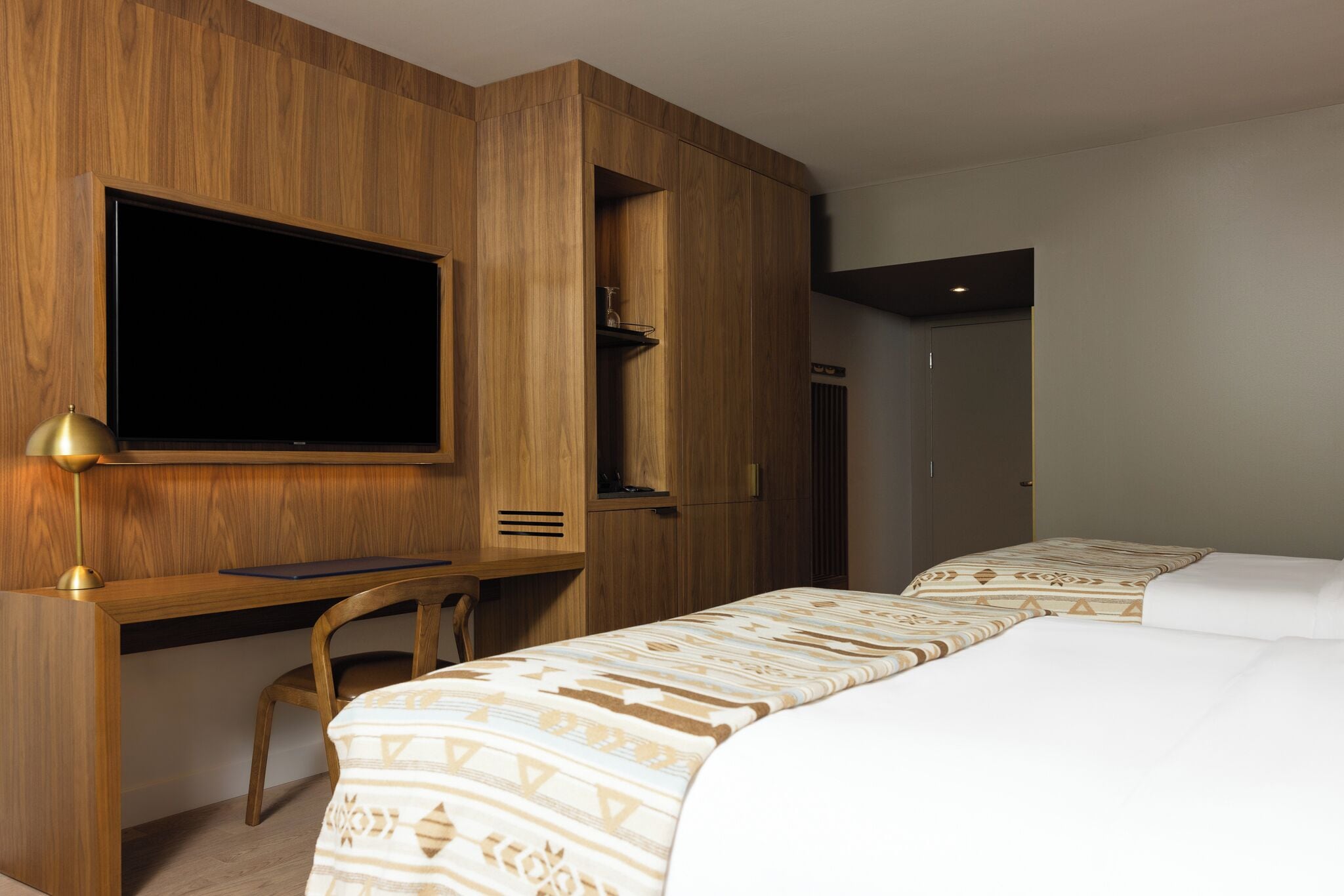 Habitación de hotel con un escritorio de madera, televisor, cama con ropa de cama estampada y armario.