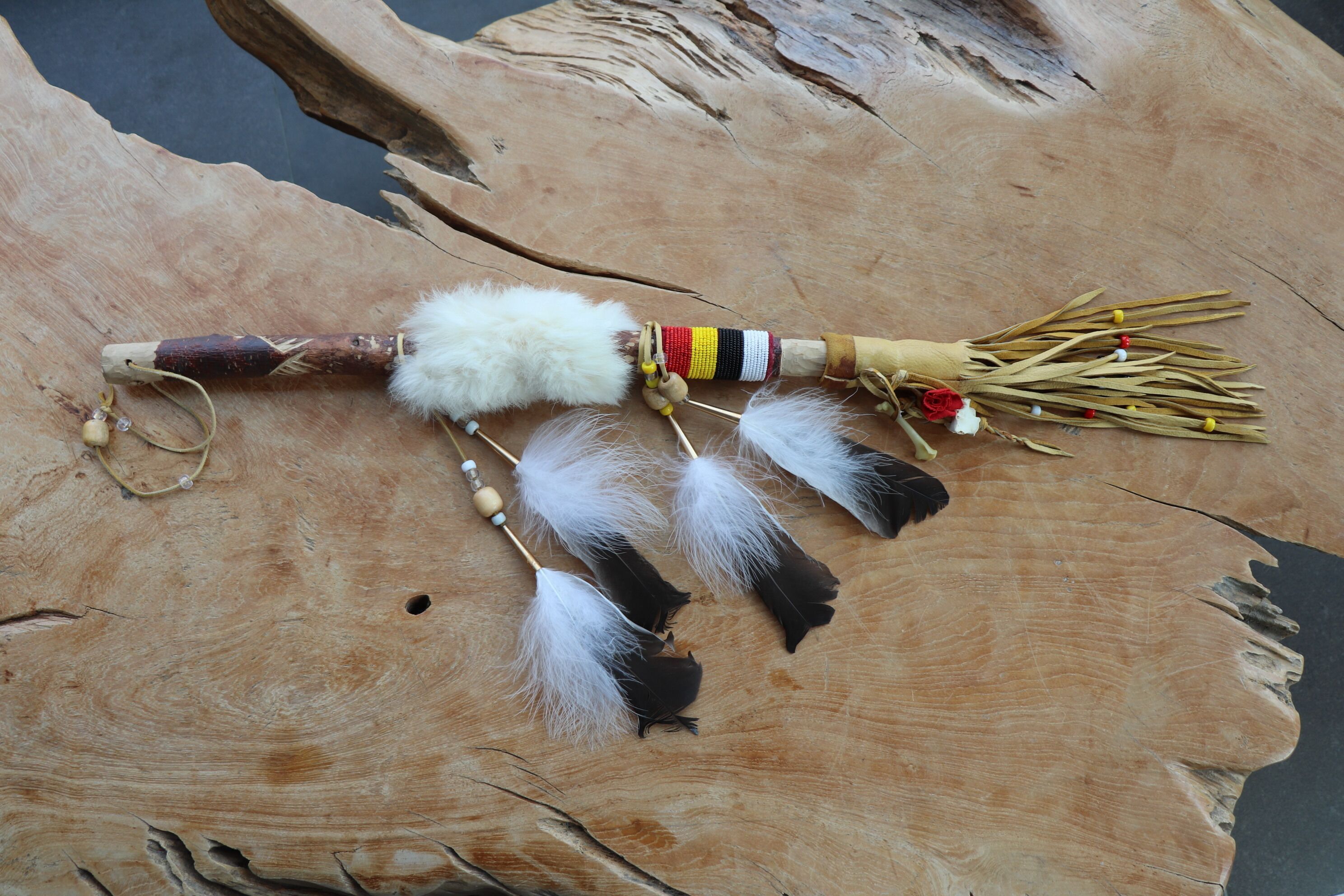 Une surface en bois ornée d’un objet décoratif composé de plumes, de perles et d’un autre objet également orné de plumes.