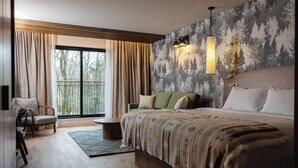 Um quarto moderno com uma cama grande, um sofá verde, piso de madeira e vista para árvores pela janela.