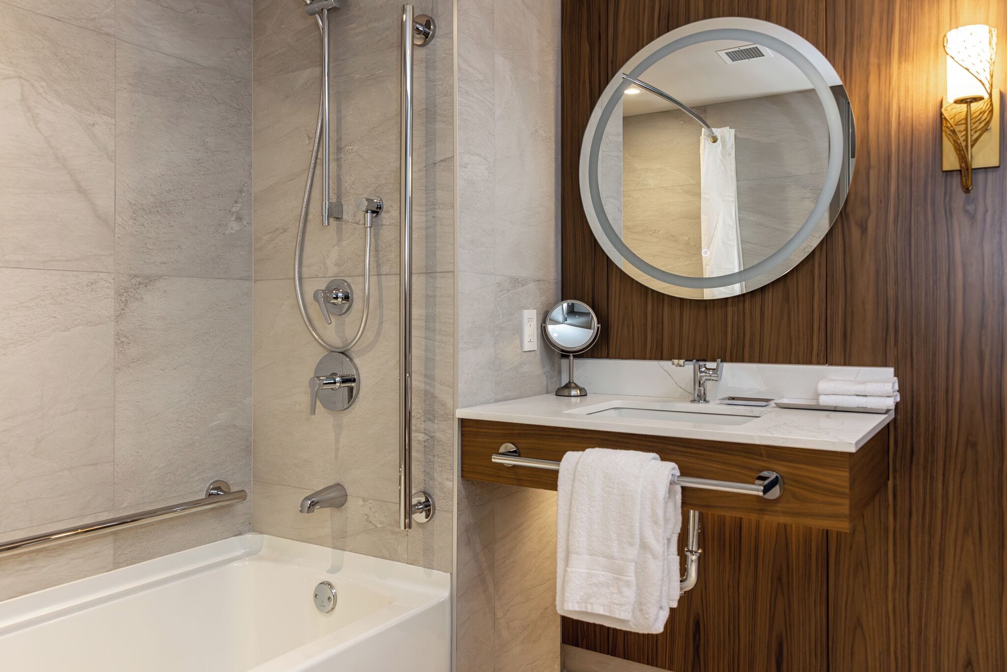 Une salle de bain moderne avec une baignoire, une douche dotée d’une porte en verre, un meuble-lavabo en bois avec un miroir et un porte-serviettes.
