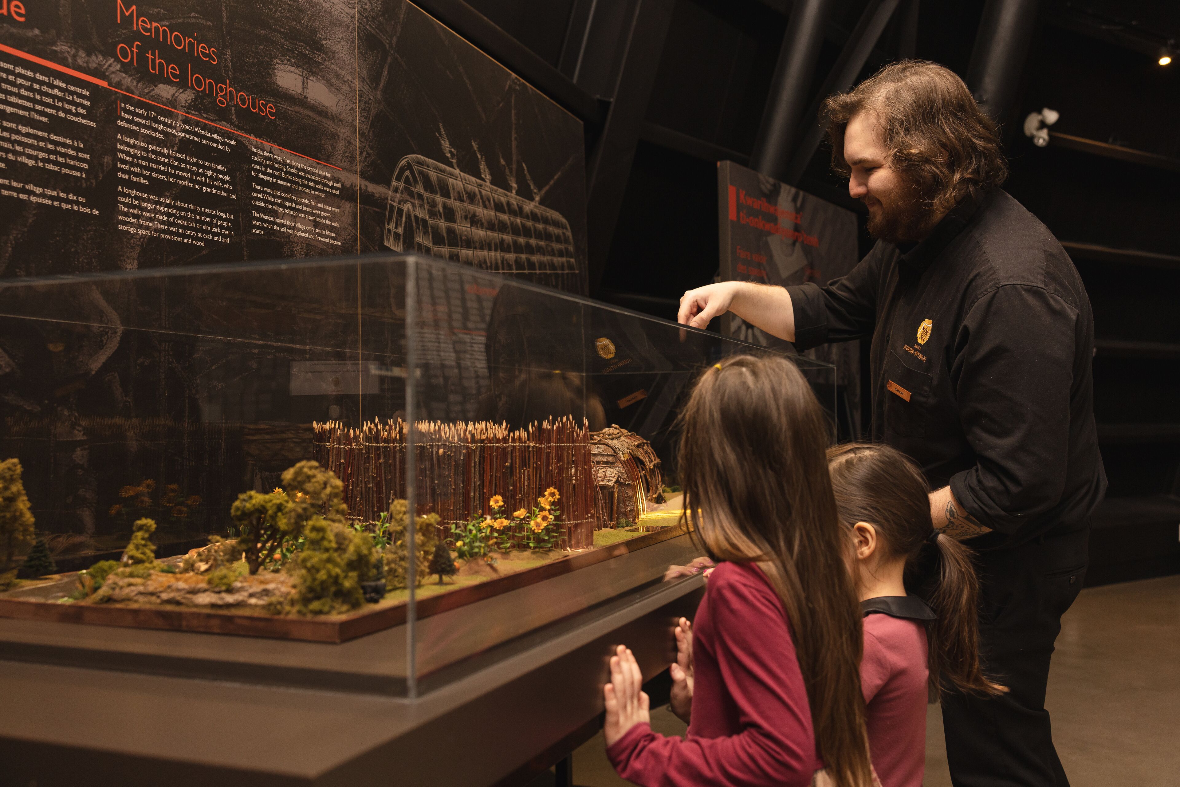 A museum exhibit with a detailed model of a longhouse, including a roof structure and surrounding landscape.