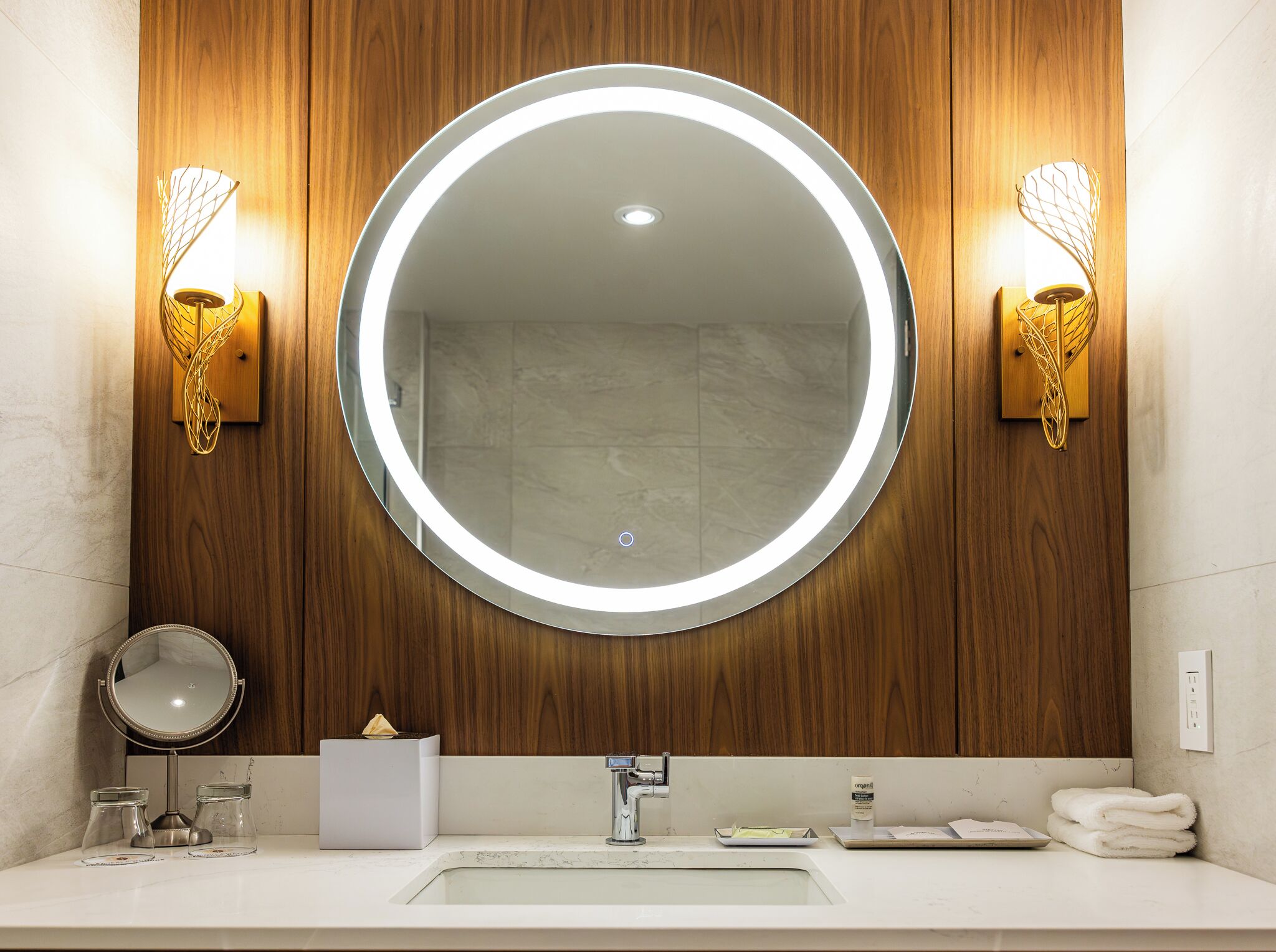 Une salle de bain avec un miroir rond, un lambris en bois, un lavabo et deux appliques murales.