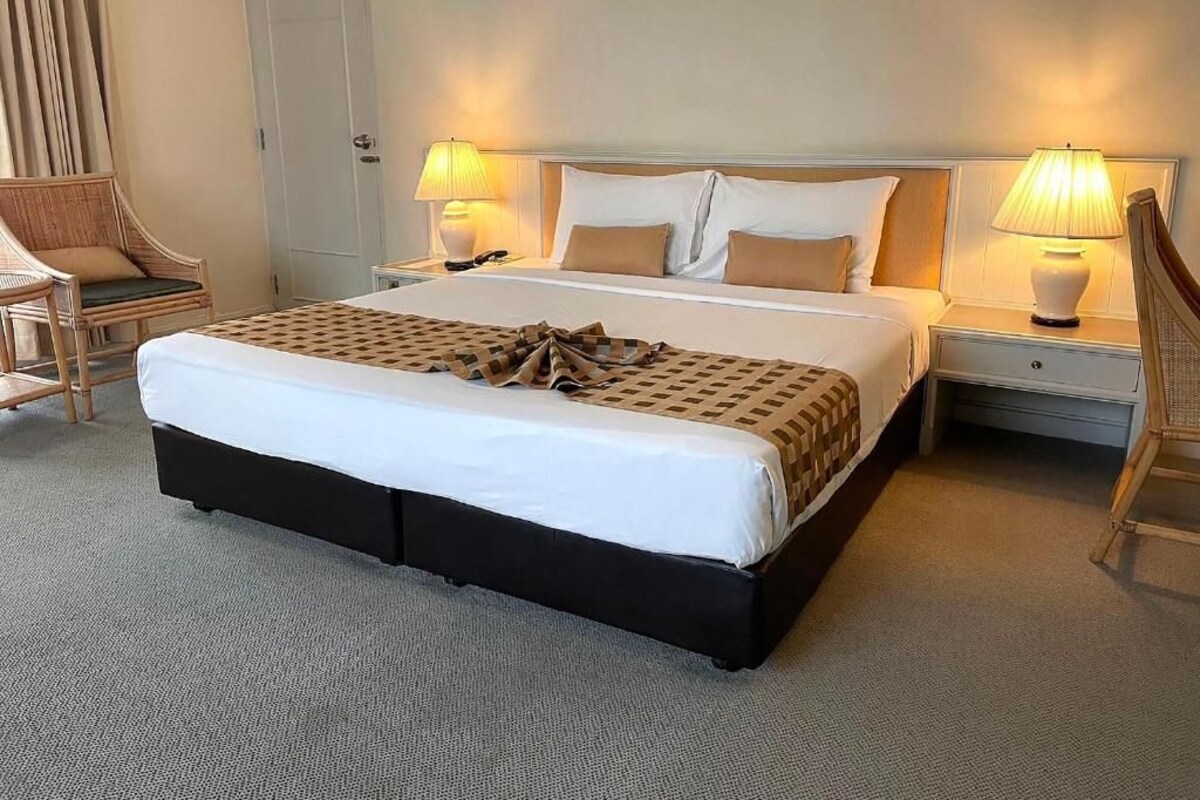 Habitació d'hotel amb un llit gran, dues taules de nit, una cadira i una làmpada.