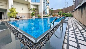 Uma piscina com borda de pedra, cercada por plantas em vasos e cadeiras de descanso.