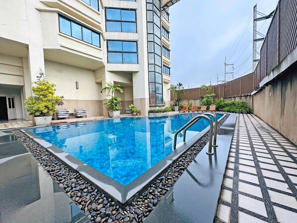 A swimming pool with a stone border, surrounded by potted plants and lounge chairs. - Lanna Palace 2004 Hotel (Chiang Mai)