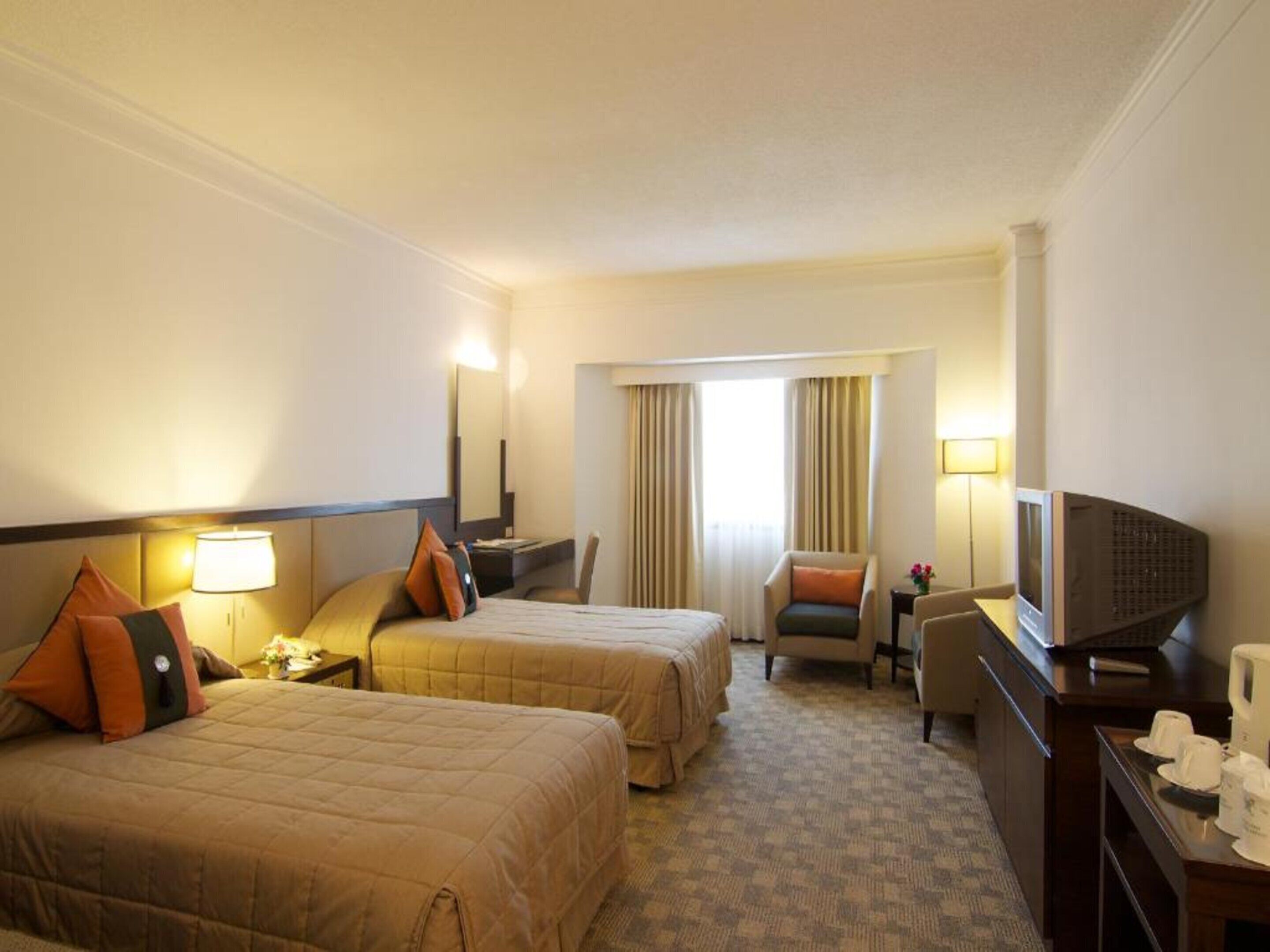 A hotel room with two beds, a desk, a chair, a television, and a window with curtains.