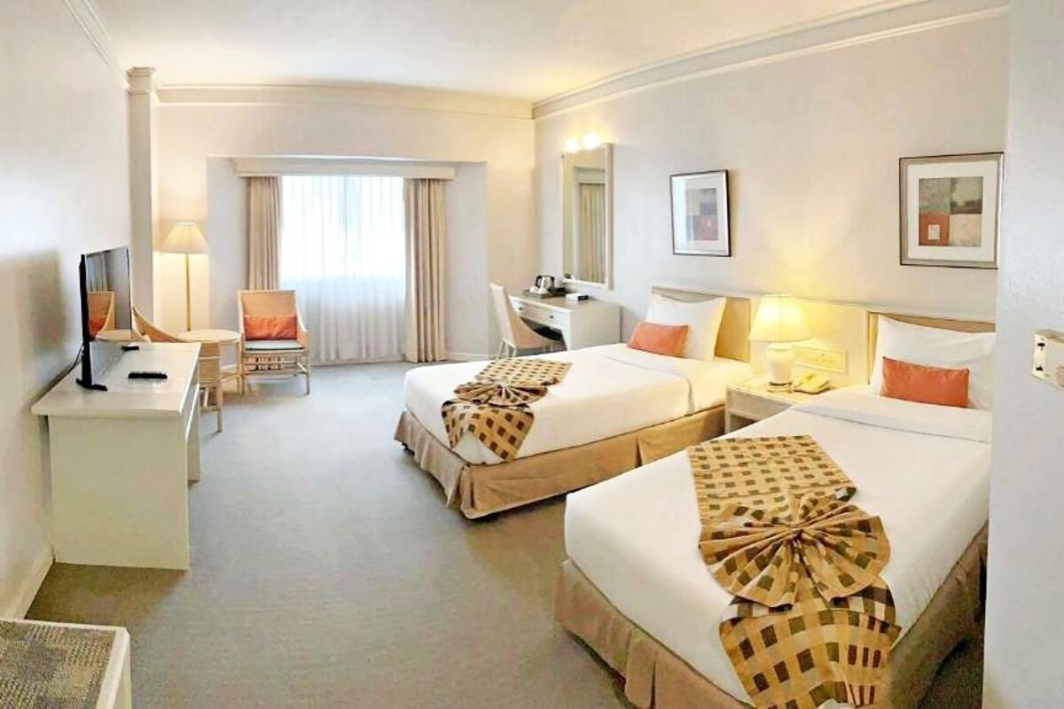 Habitació d'hotel amb dos llits, una taula de treball, una cadira i una finestra amb cortines.