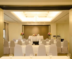 A conference room with rows of tables and chairs, a stage with a podium, and a chandelier.