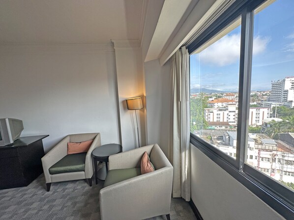 Habitación de hotel con dos sillones, una mesita, una lámpara y un ventanal con vistas a la ciudad.