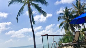 A poolside area with a clear view of the ocean, palm trees, and a blue umbrella. - Royal Beach Boutique Resort & Spa (Koh Samui)