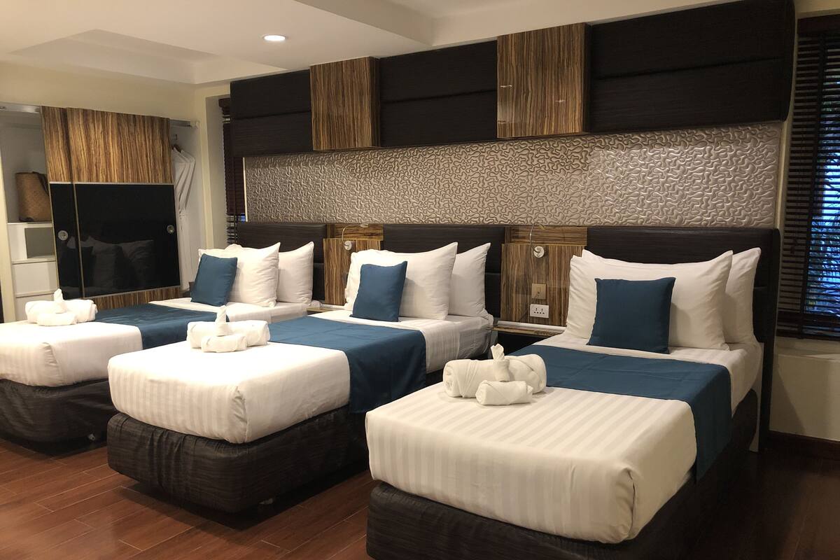 A hotel room with four beds arranged in a row, each with a pillow and a towel.