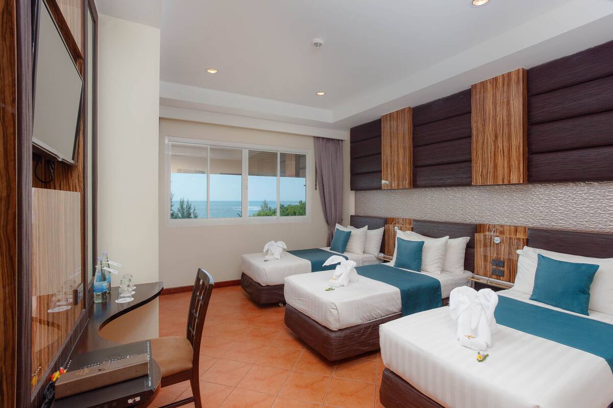 A hotel room with two beds, a desk, and a large window offering a view of the sea.