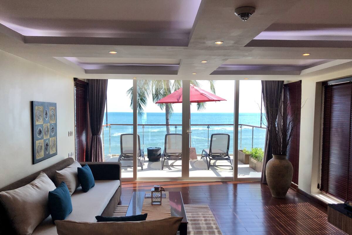 A spacious living room with a large sofa, a coffee table, and a view of the ocean through large glass doors.
