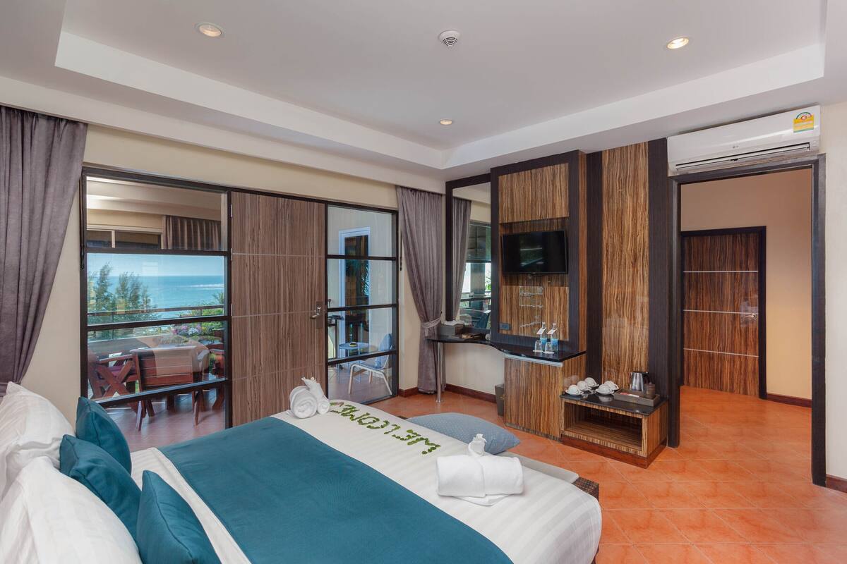 A hotel room with a large bed, a desk with a TV, and a view of the outdoors.