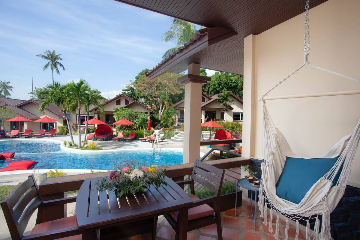 A poolside area with a hammock, lounge chairs, and a table with flowers.