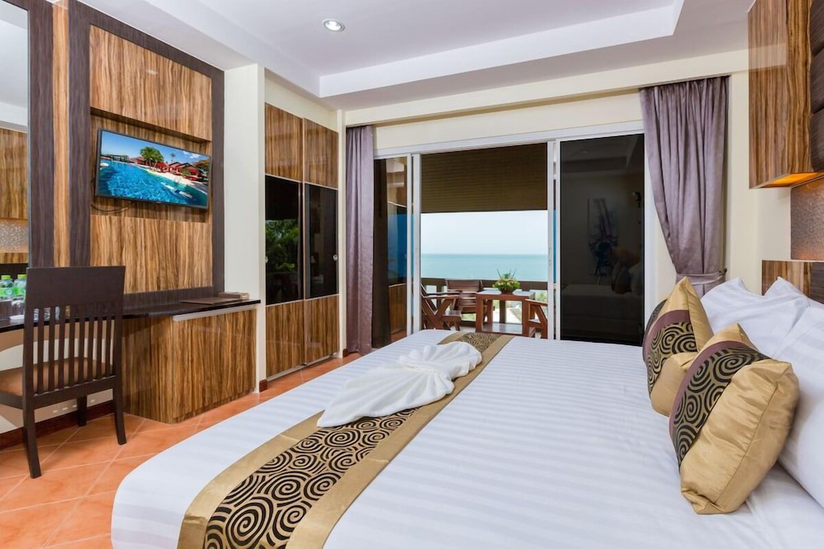 A hotel room with a bed, a desk, a television, and a view of the ocean.