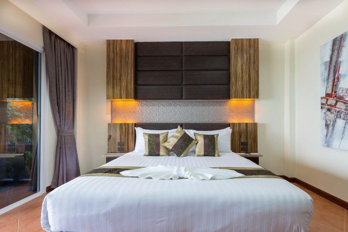 A hotel room with a large bed, a headboard with built-in lighting, and a view through a glass door.