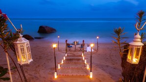 A beach setting with a pathway leading to a table and chairs, surrounded by lanterns and plants. - Royal Beach Boutique Resort & Spa (Koh Samui)