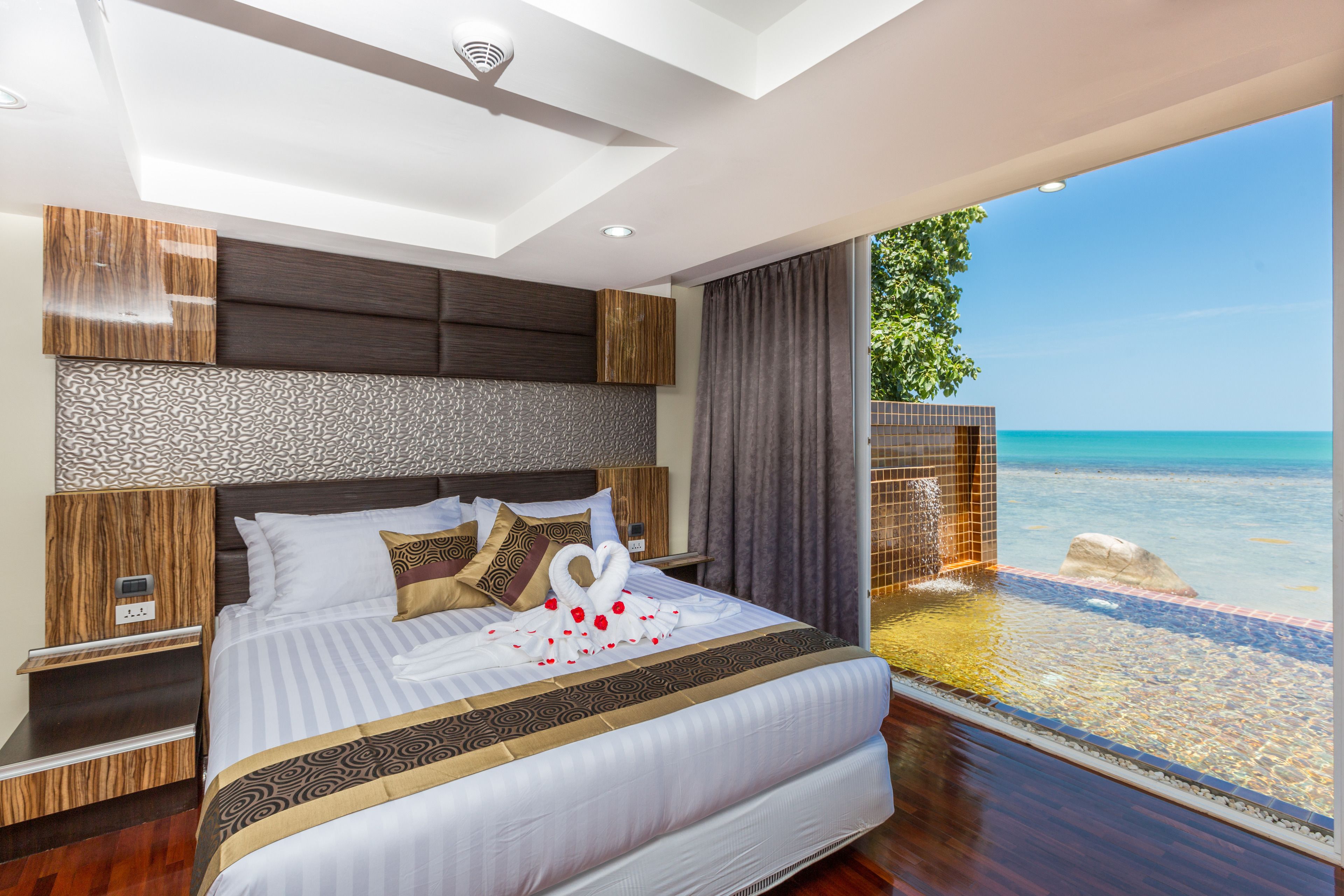 Een moderne hotelkamer met een groot bed, uitzicht op zee en een balkon met een zwembad.