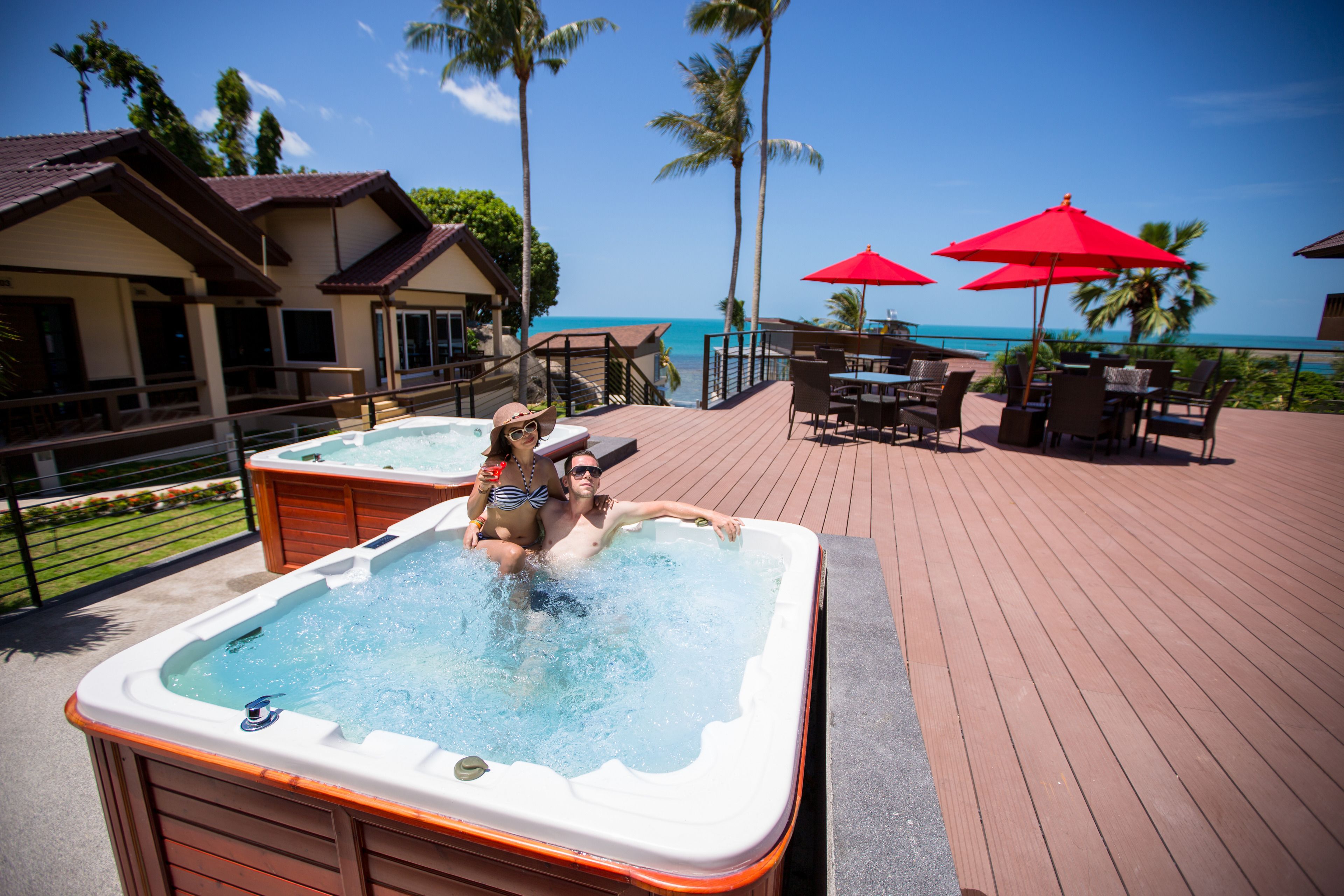 Uma banheira de hidromassagem em um deck de madeira, com vista para o oceano e palmeiras.