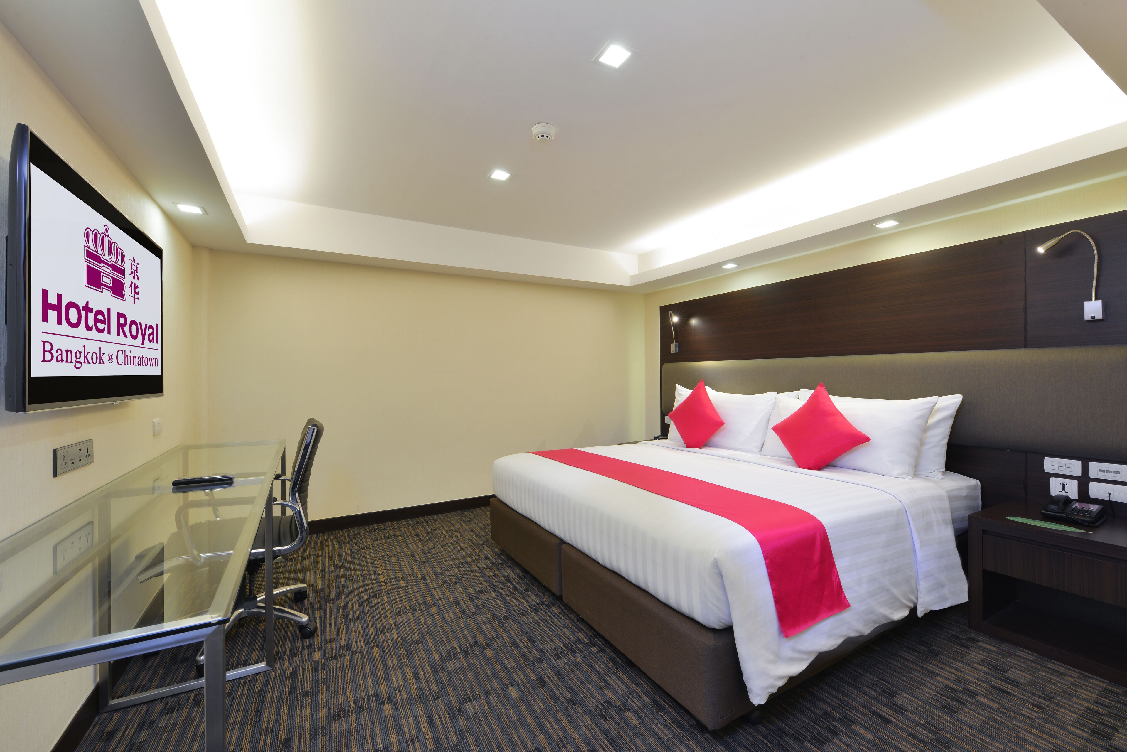 Una habitación de hotel con una cama grande, una mesita de vidrio y un cabecero con una lámpara.