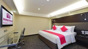 Una habitación de hotel con una cama grande, una mesita de vidrio y un cabecero con una lámpara.
