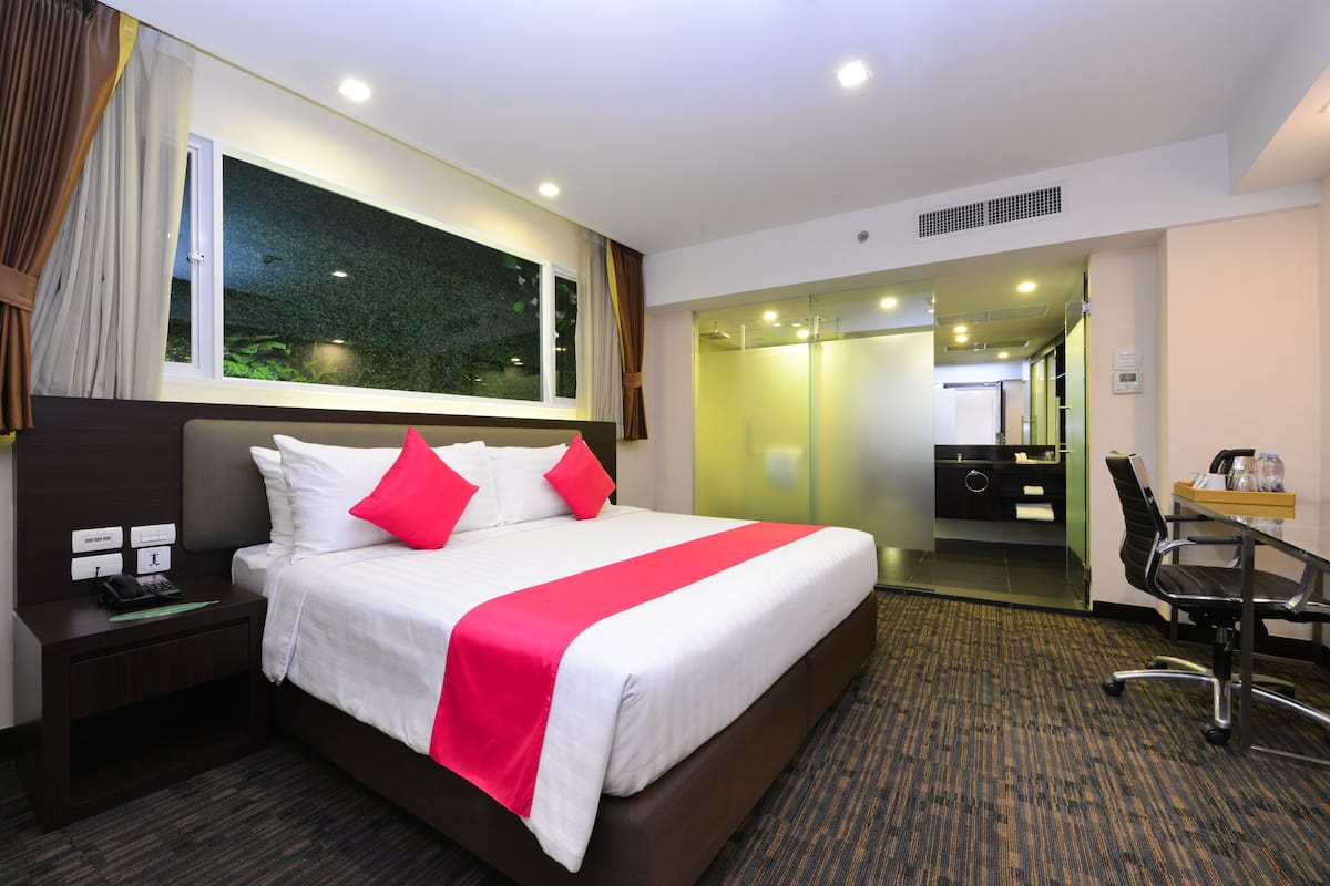 Une chambre d’hôtel avec un grand lit, un bureau avec une chaise, un téléphone et une fenêtre avec des rideaux.