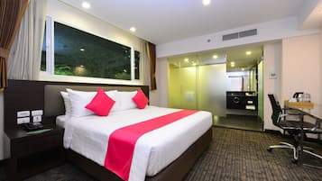 Habitación de hotel con una cama grande, un escritorio con silla, teléfono y una ventana con cortinas.