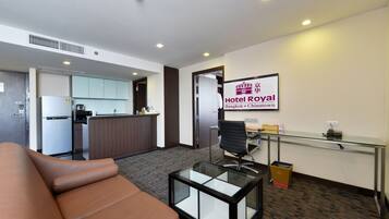 A modern hotel lobby with a sofa, a glass-top coffee table, a reception desk, and a kitchen area in the background.