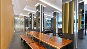A modern interior with a long wooden table and benches, recessed lighting, and a stone wall in the background. - Hotel Royal Bangkok (Bangkok)