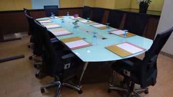Una sala de conferencias con una mesa de vidrio, sillas negras y una planta en maceta.