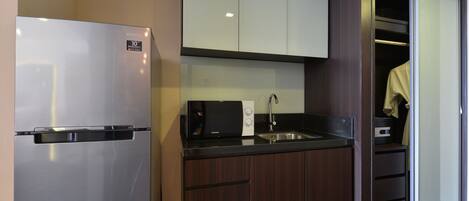 Una cocina compacta con refrigerador de acero inoxidable, microondas y pileta.