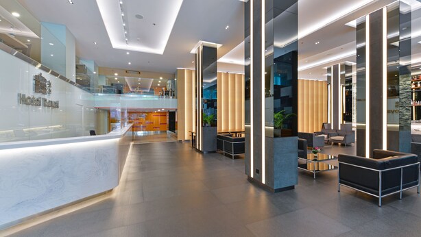 A modern hotel lobby with a reception desk, seating area, and a staircase leading to an upper level. - Hotel Royal Bangkok (Bangkok)