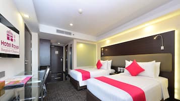Quarto de hotel com duas camas, uma escrivaninha e uma televisão exibindo o nome do hotel.