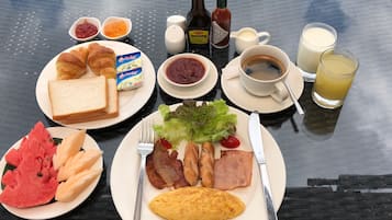 A breakfast table with croissants, toast, ham, eggs, and fruit. There are condiments, coffee, and a glass of juice.