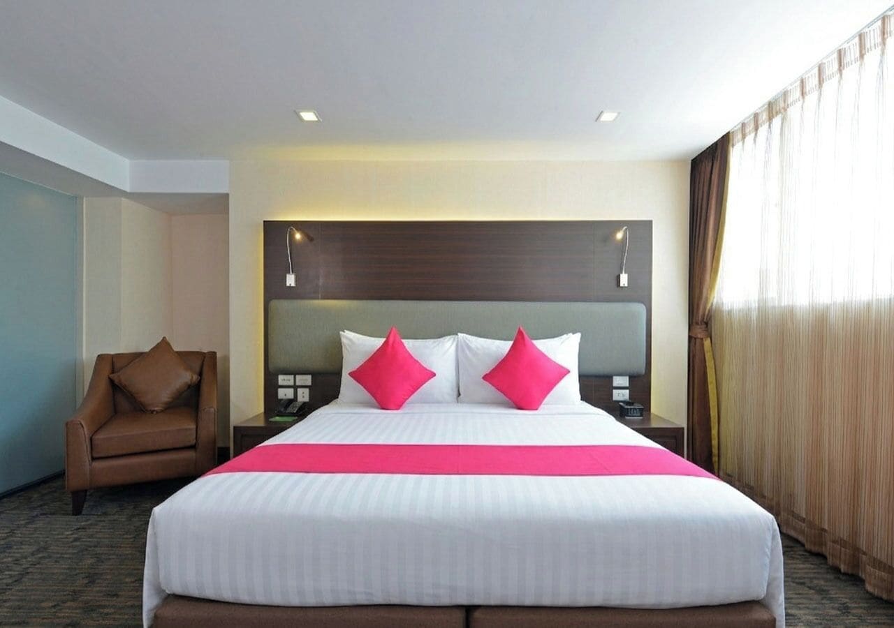 A hotel room with a large bed, two bedside tables, a chair, and a window with curtains.