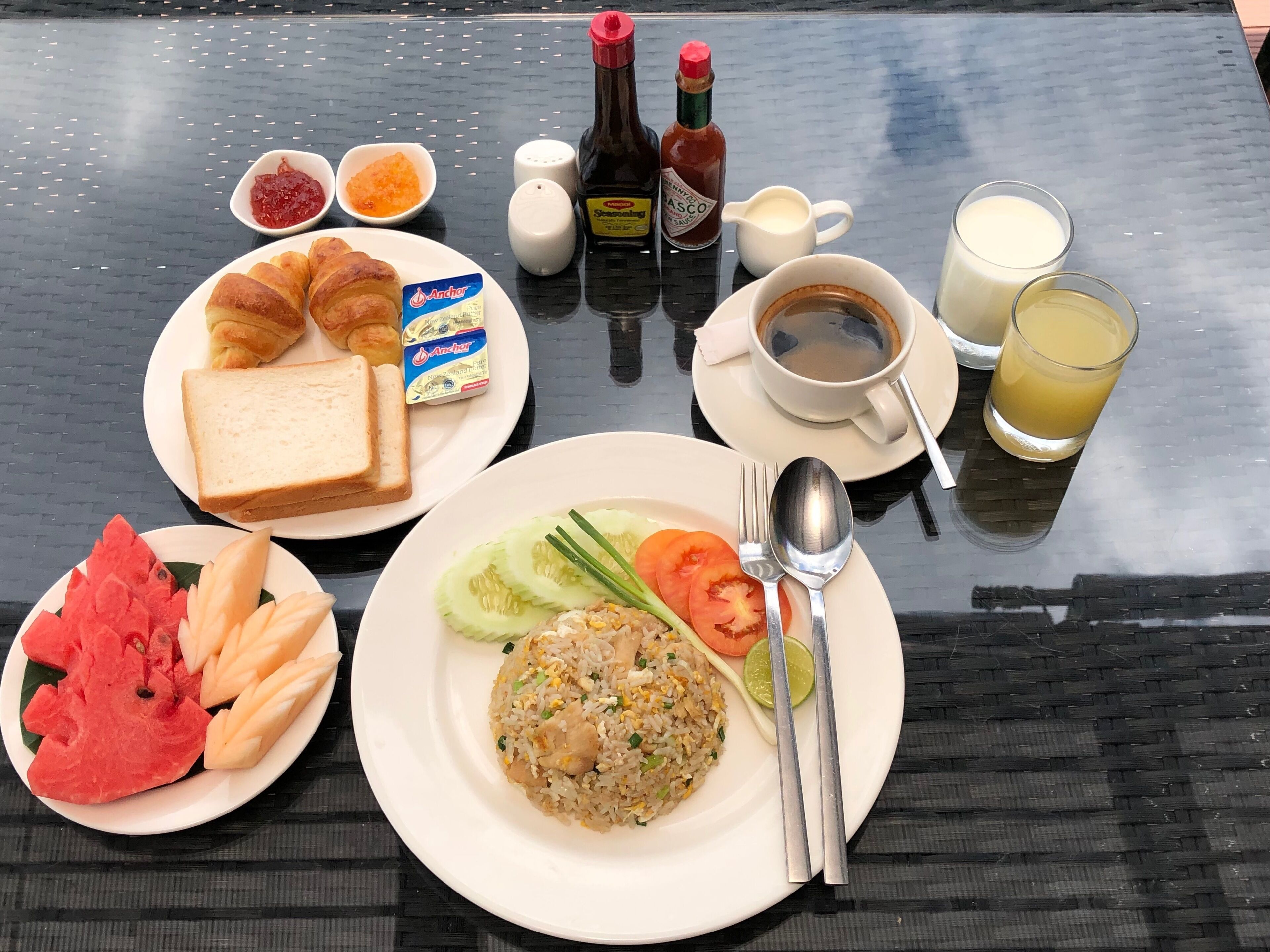 A breakfast table with croissants, toast, fruit, fried rice, and beverages.