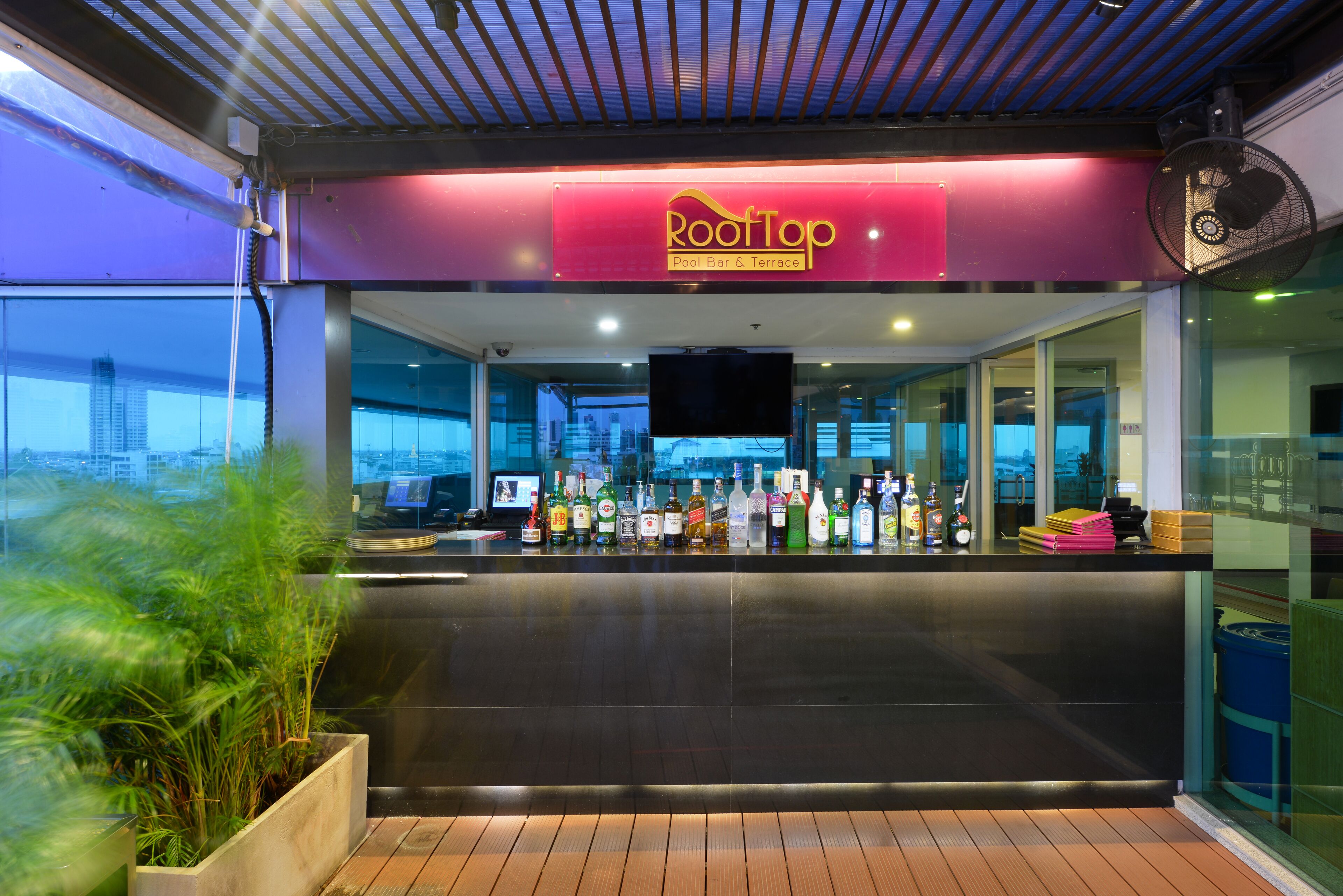 A bar area with a sign reading "RootTop Pool Bar & Terrace" and a variety of bottles on the counter.