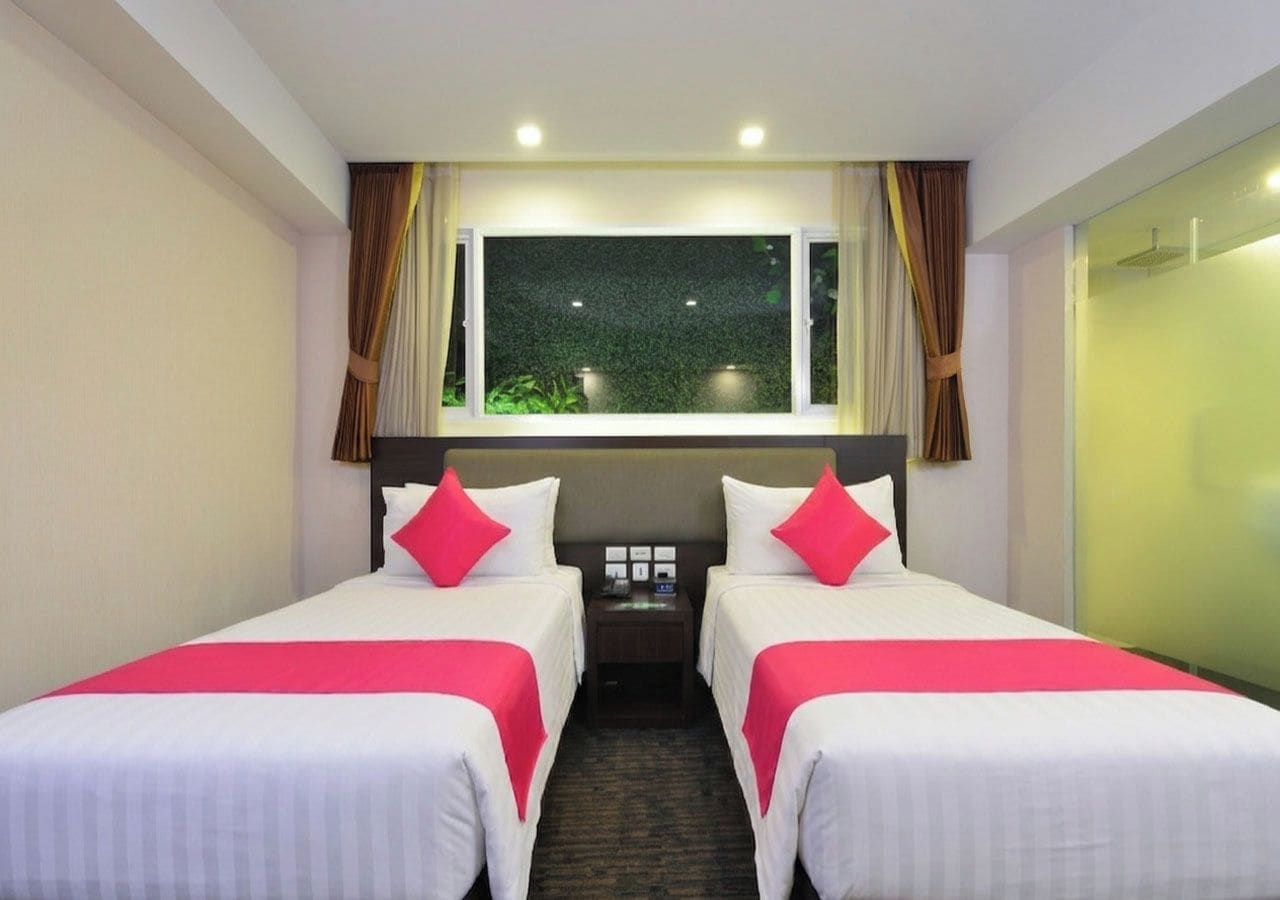 Habitación de hotel con dos camas, una mesita de noche, una ventana con cortinas y un rincón de ducha.