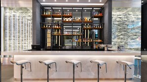 A bar area with multiple shelves of bottles, a marble countertop, and four bar stools. - Hotel Royal Bangkok (Bangkok)