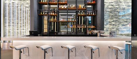 Una zona de bar con varias estanterías llenas de botellas, una encimera de mármol y cuatro taburetes de bar.