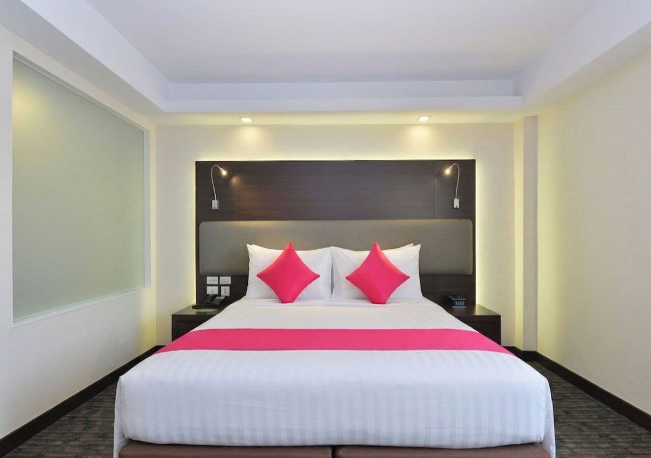 Una habitación de hotel con una cama grande, dos mesitas de noche y un cabecero con iluminación integrada.